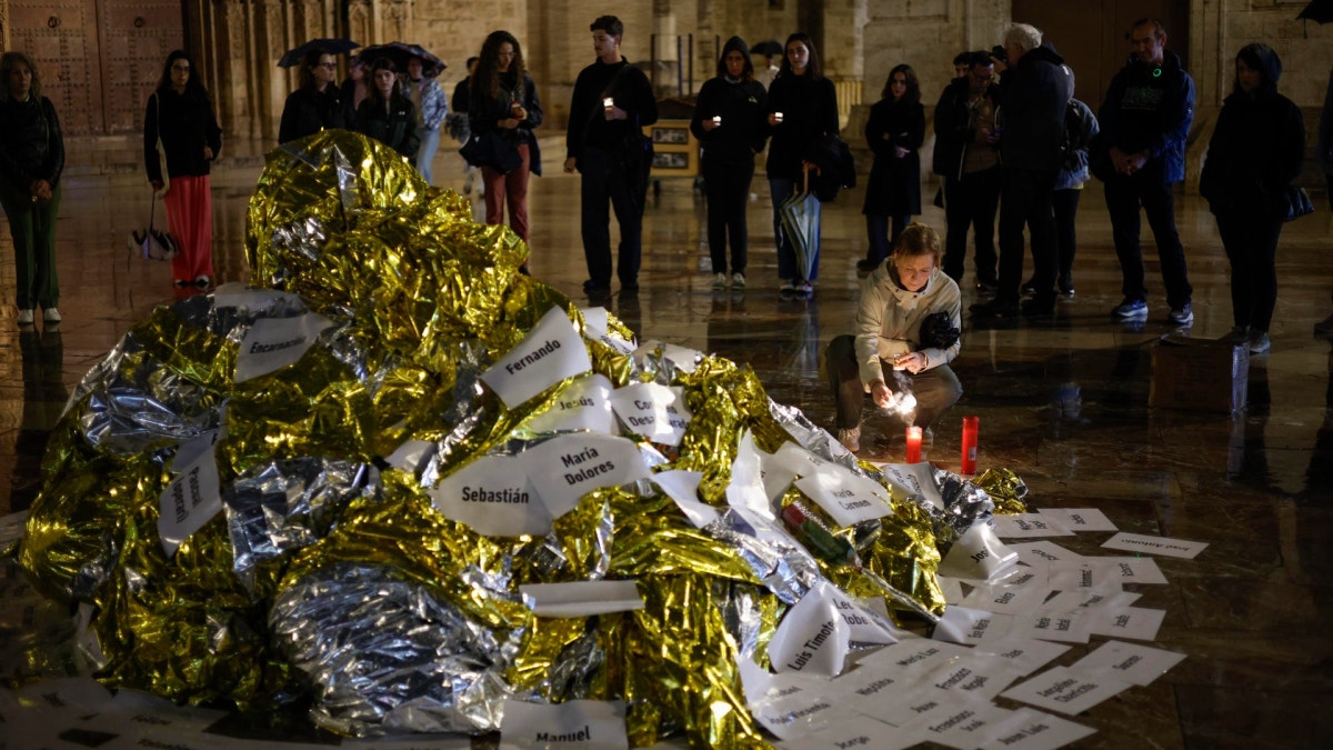Varias personas colocan velas en un altar improvisado en el acto de denuncia y homenaje a las víctimas de la dana en el que 229 mantas térmicas tapizan la plaza de la Virgen en memoria de los que perdieron la vida en la tragedia