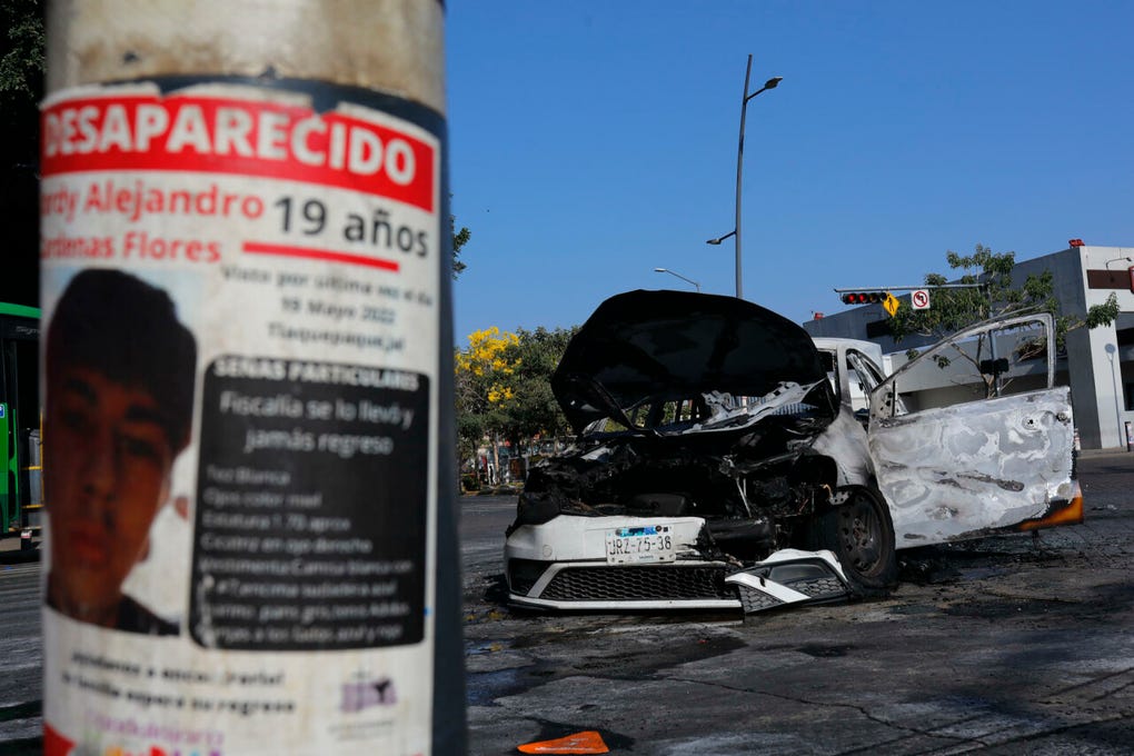 Fotografía que muestra un cartel de una persona desaparecida y un vehículo incendiado este domingo, en una vía de Guadalajara (México).