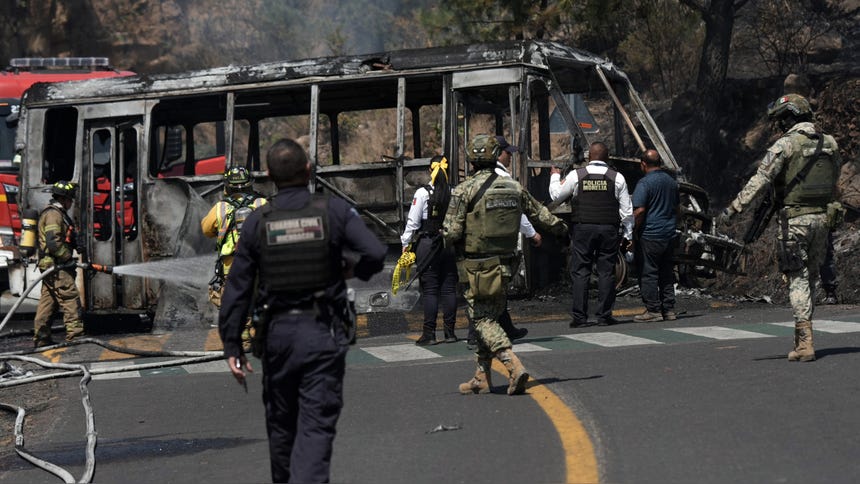 Bomberos y agentes de la Policía atienden la emergencia de un bus incenciado por presuntos integrantes del CJNG en Morelia. 