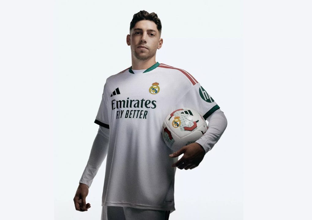 El blanco de la camiseta se combina con detalles en verde oscuro en el cuello y los puños de las mangas.
