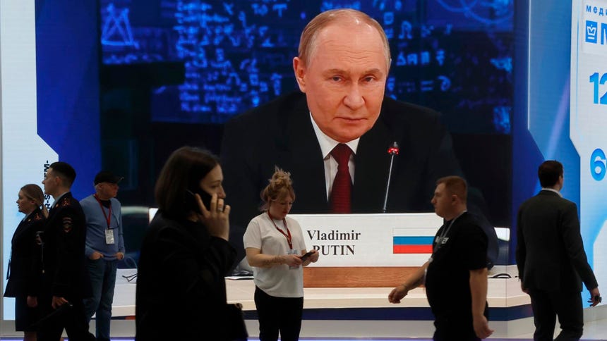 Asistentes del foro pasan junto a una gran pantalla que muestra una imagen del presidente ruso Vladimir Putin. 
