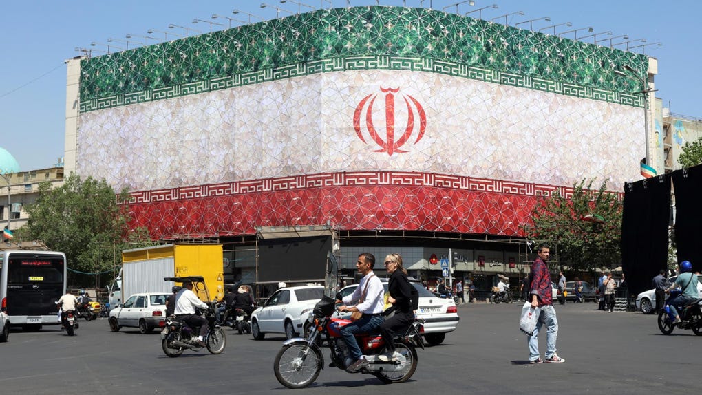 Conductores iraníes pasan en coche junto a una valla publicitaria con la bandera nacional de Irán en la plaza Enqelab de Teherán, Irán.