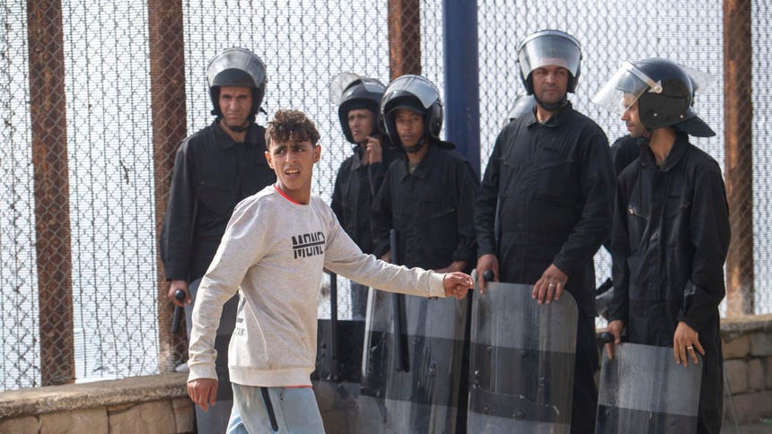 Un marroquí camina al costado de miembros de seguridad de Marruecos, en medio del retorno de marroquís que intentaron llegar hasta la ciudad española de Ceuta.