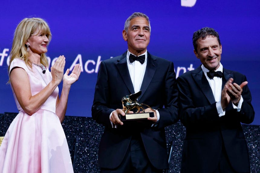 George Clooney recibe el León de Oro a la trayectoria profesional de manos de la actriz estadounidense Laura Dern y del presidente de la Bienal, Pietrangelo Buttafuoco.    