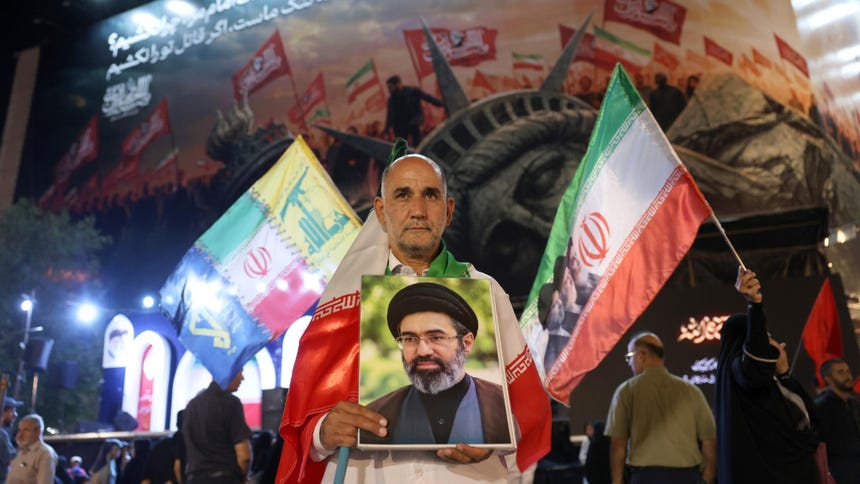 Un hombre iraní (izquierda) sostiene un retrato del líder supremo, el ayatolá Mojtaba Jamenei, durante una manifestación nocturna contra Estados Unidos celebrada en Teherán, Irán, el 26 de agosto de 2026, tras el anuncio de nuevas sanciones por parte de Washington.